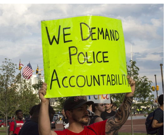 demonstrators hold up day glow green sign saying "we demand police accountability" 