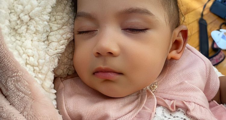 Dark-skinned infant girl sleeping in pink outfit and flannel coat during Sunday service