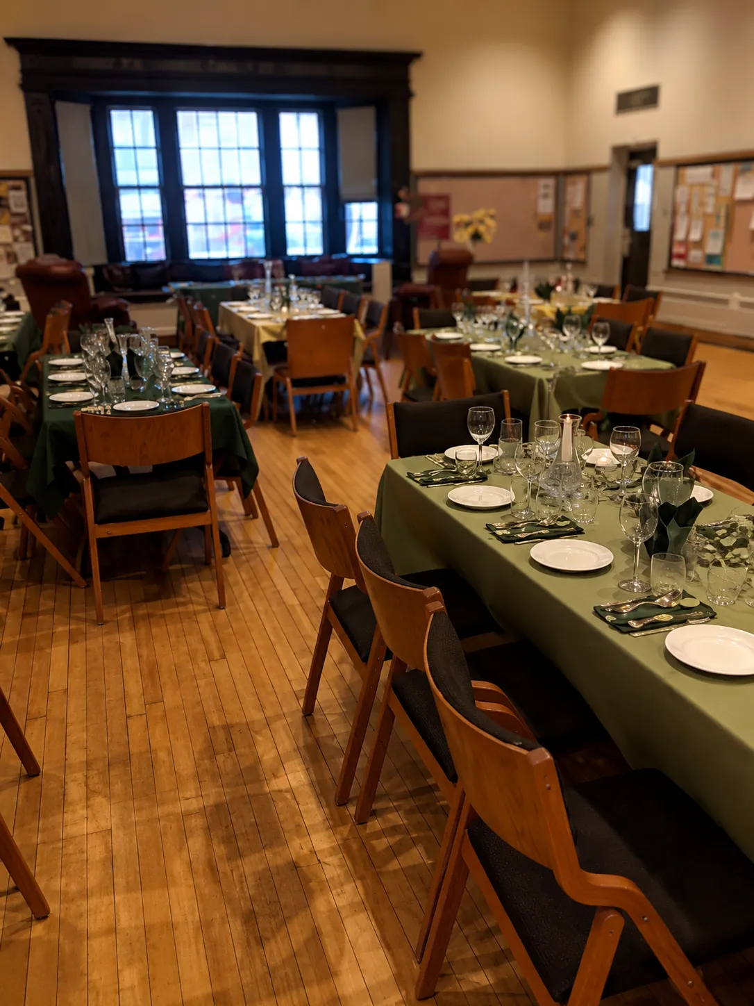 A banquet hall set with green tablecloths, glassware, and place settings