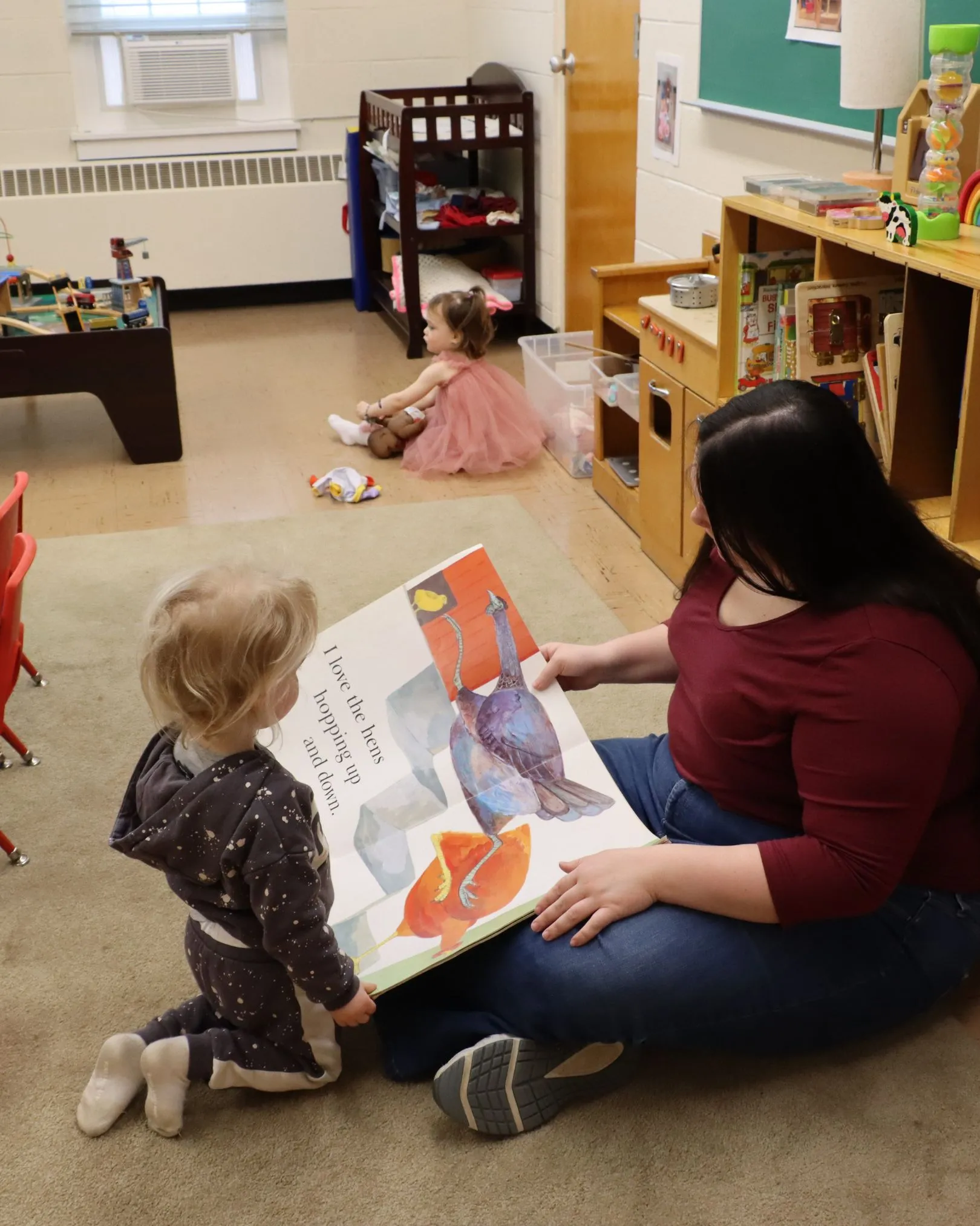 A toddler and caregiver reading a picture book together on the floor of a nursery