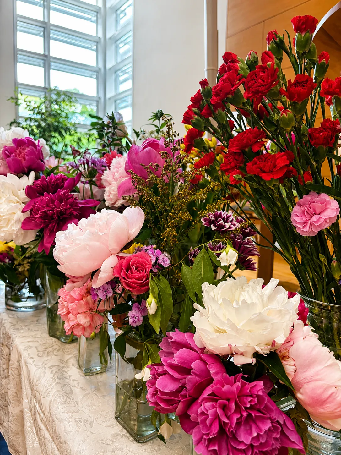 Rows of colorful peony, rose, and carnation bouquets in glass vases on a table