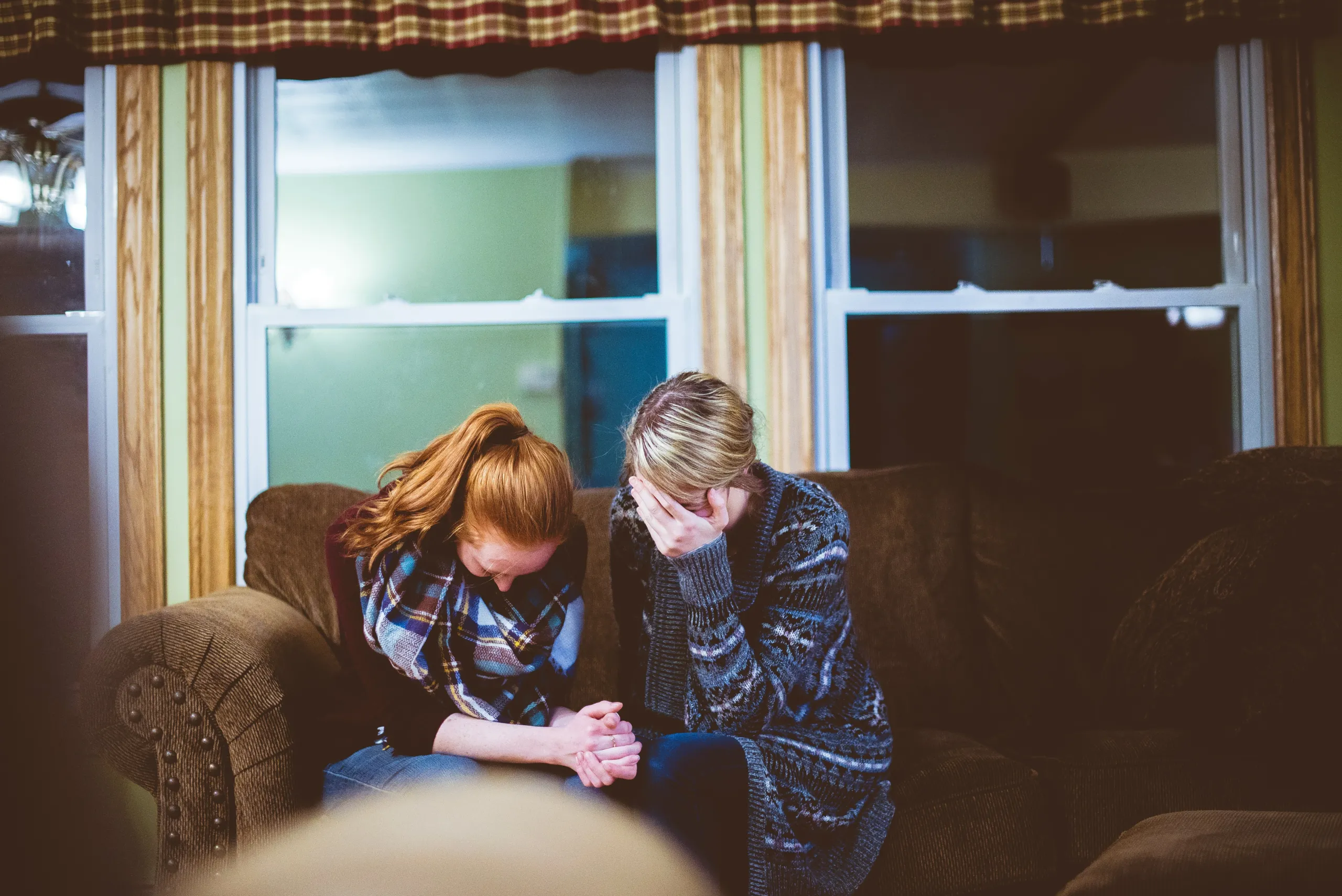 Two women sitting together on a couch, one comforting the other with a hand on her face