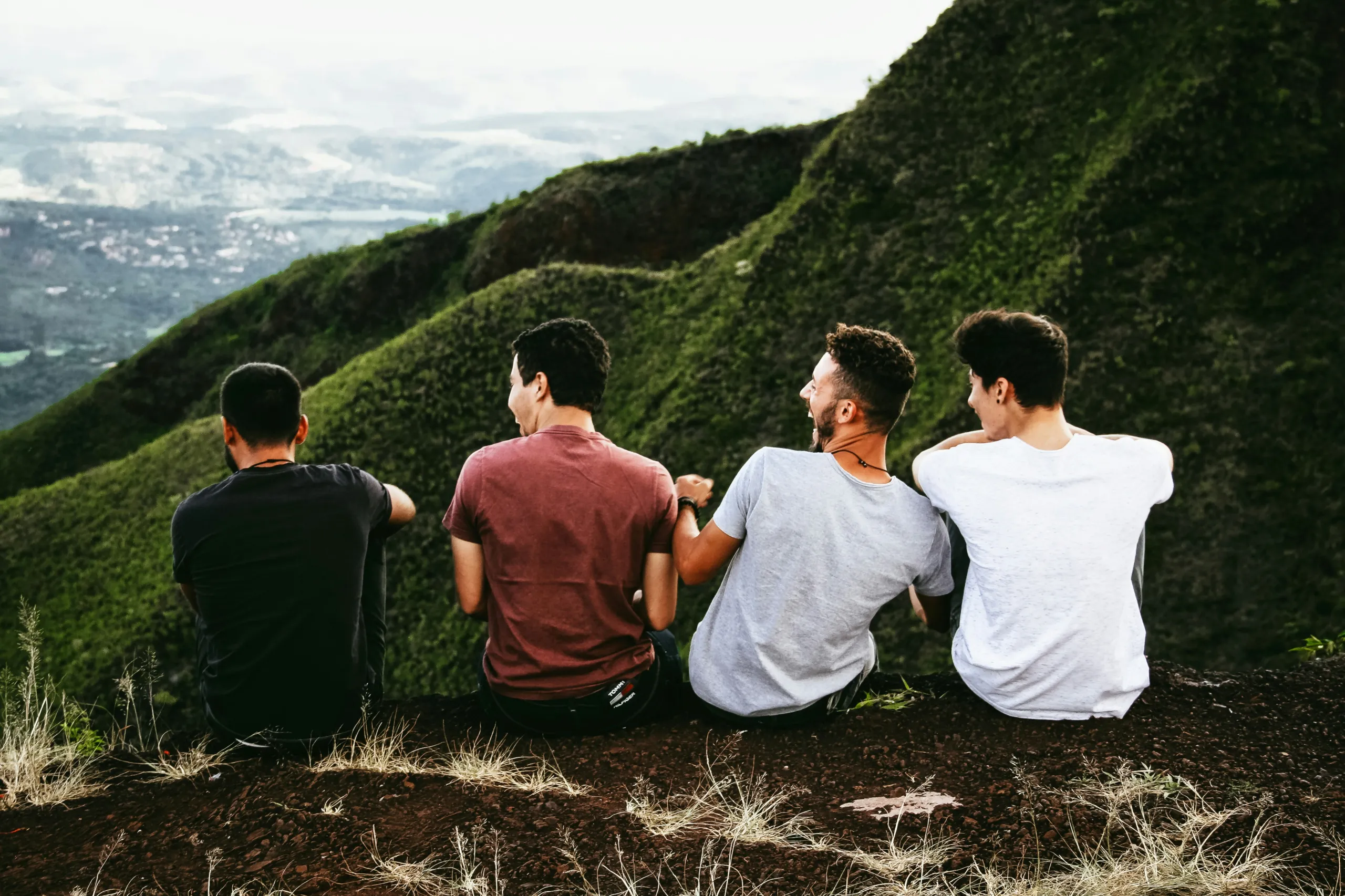 Four friends sitting with their backs to the camera, overlooking a green mountain valley
