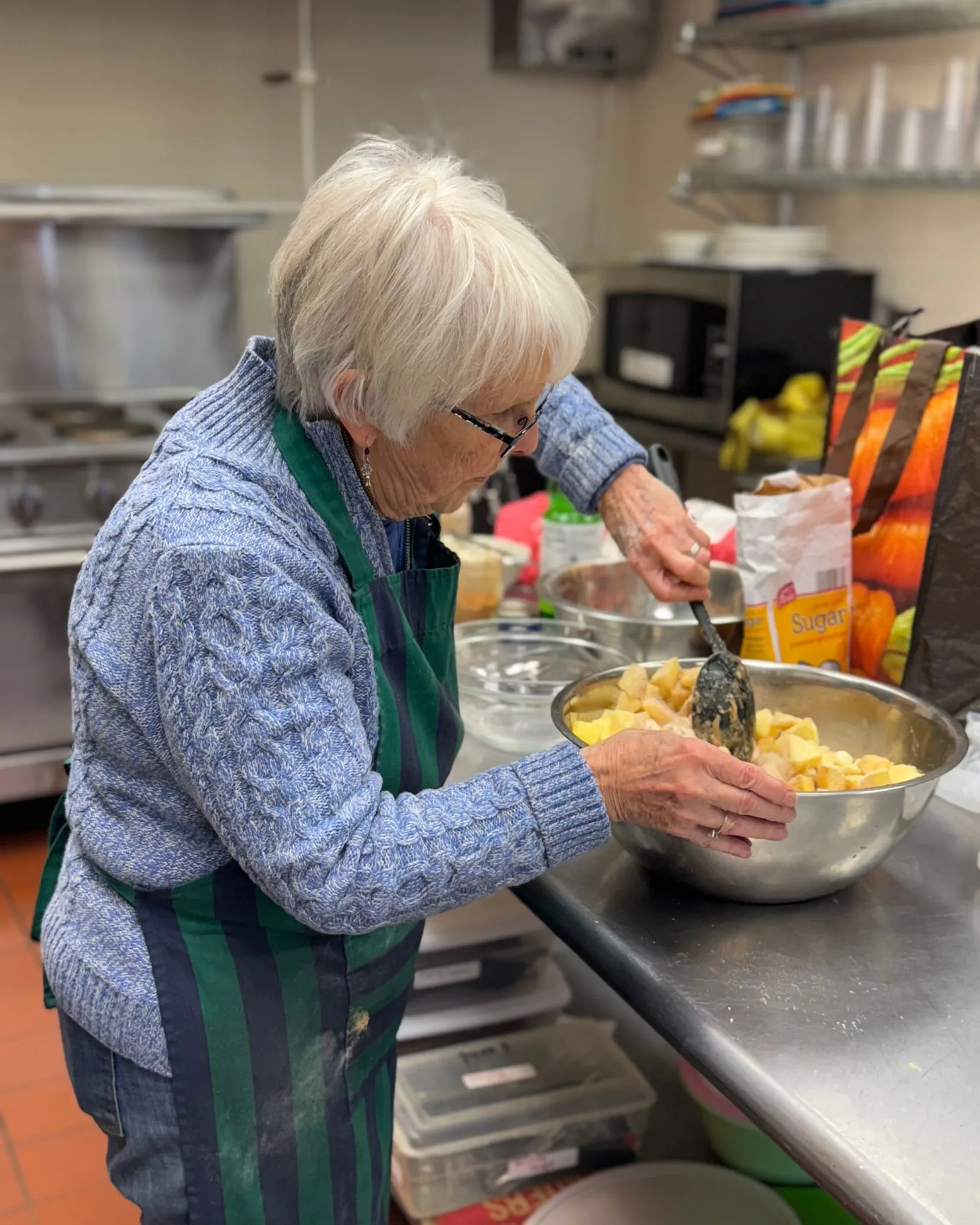 A volunteer mixing chopped apples in a bowl while baking pies in a kitchen