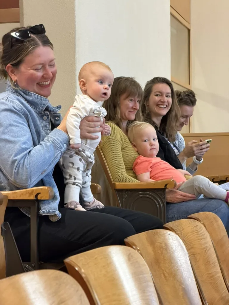 Several women holding babies and toddlers, smiling together in a row of seats