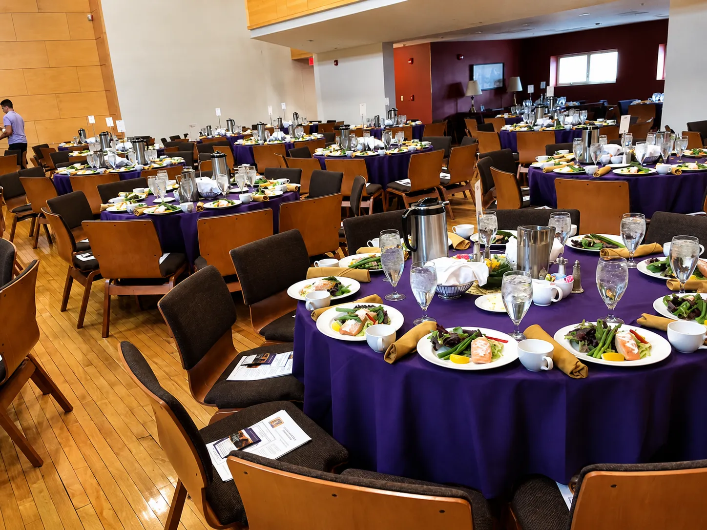 Round tables set with salmon dinner plates and purple tablecloths in a banquet hall