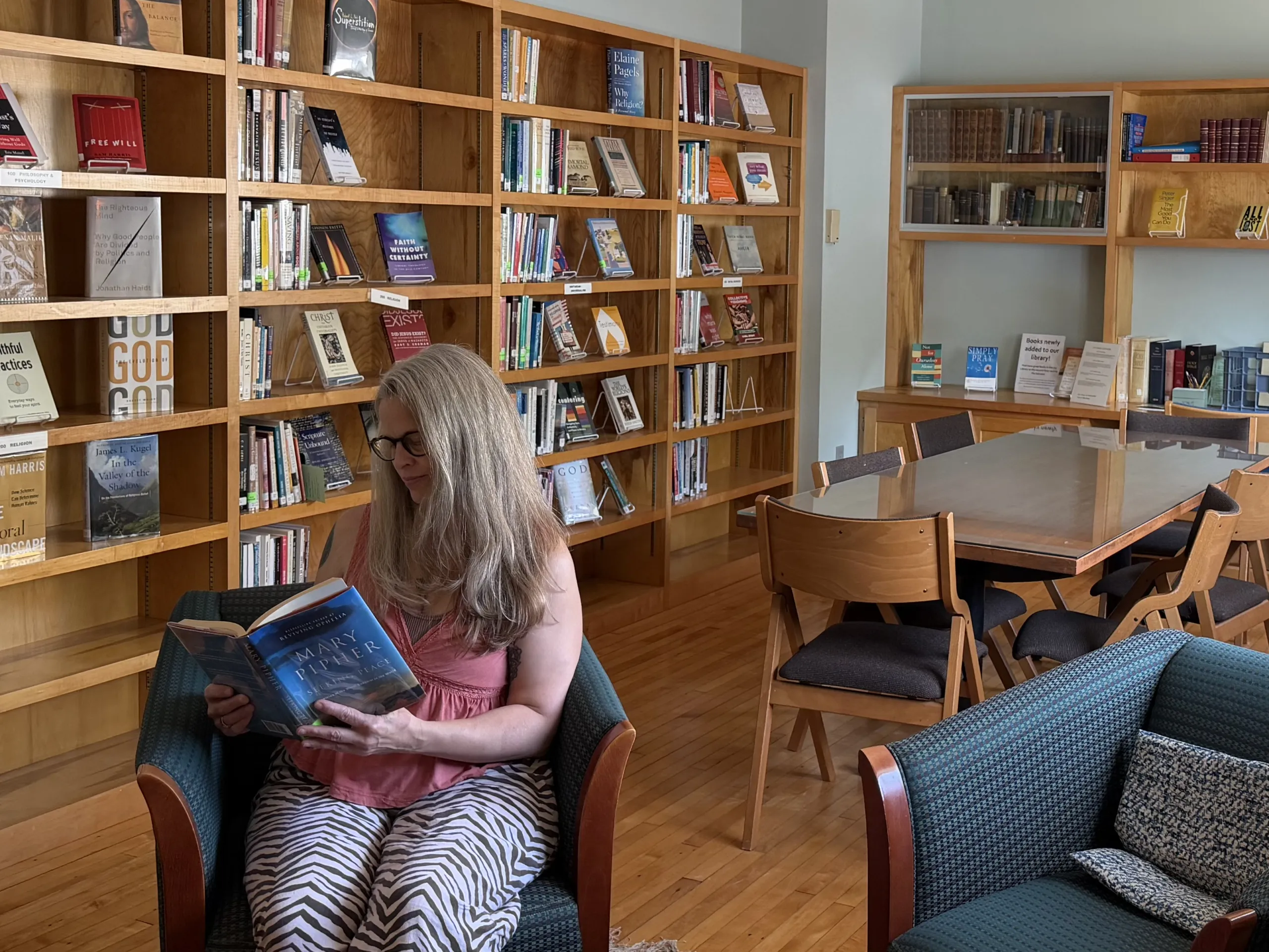 A woman reading in an armchair in the church library with a reading table nearby