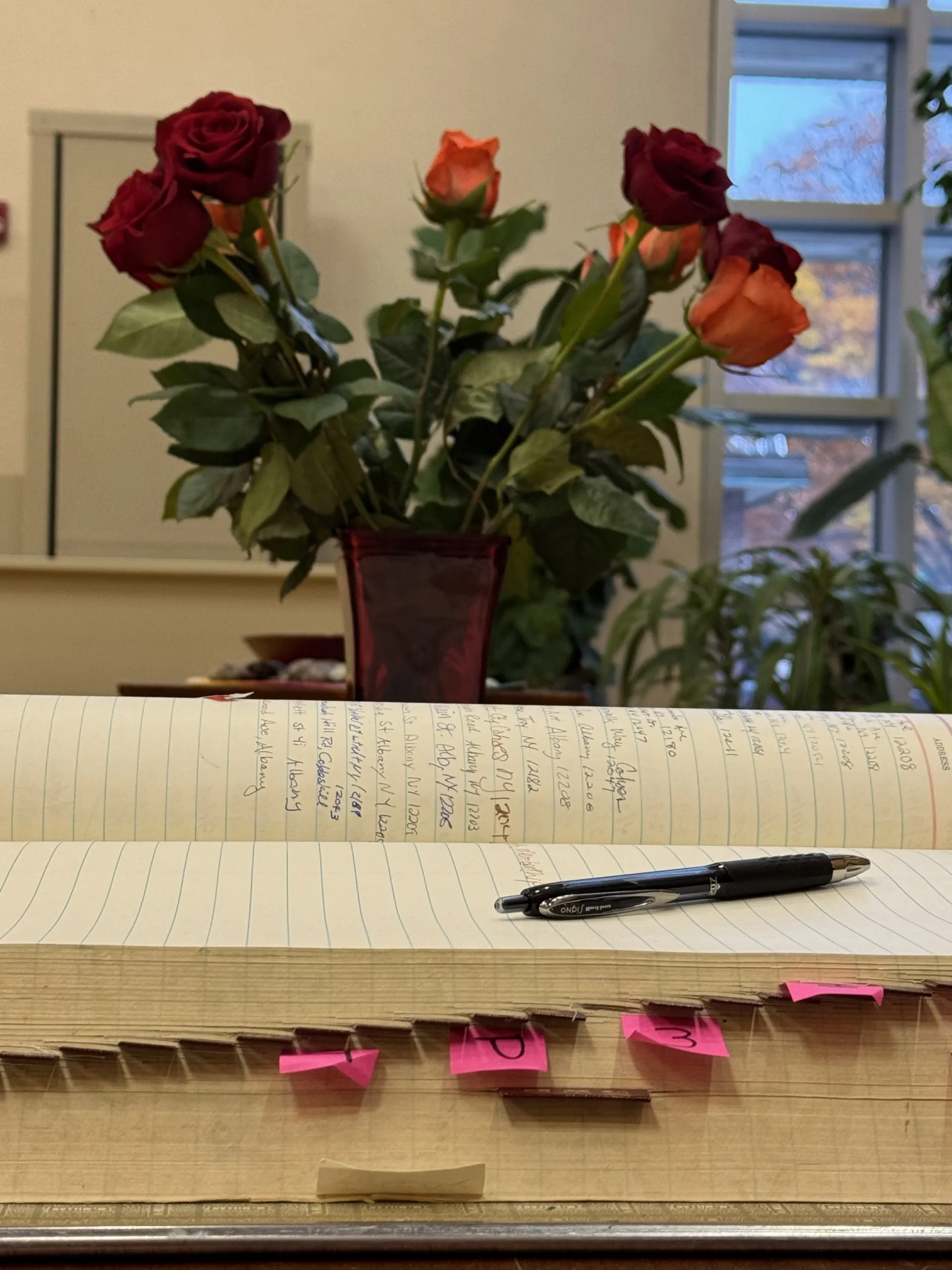 Red and orange roses in a vase beside an open guest book and pen