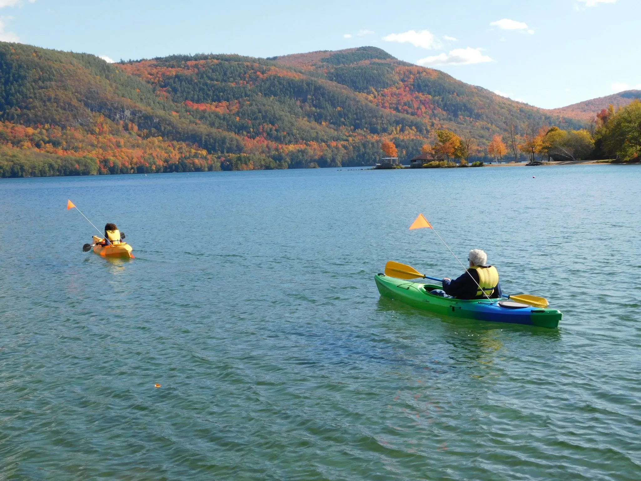 Two kayakers paddling on a lake with mountains in fall foliage in the background