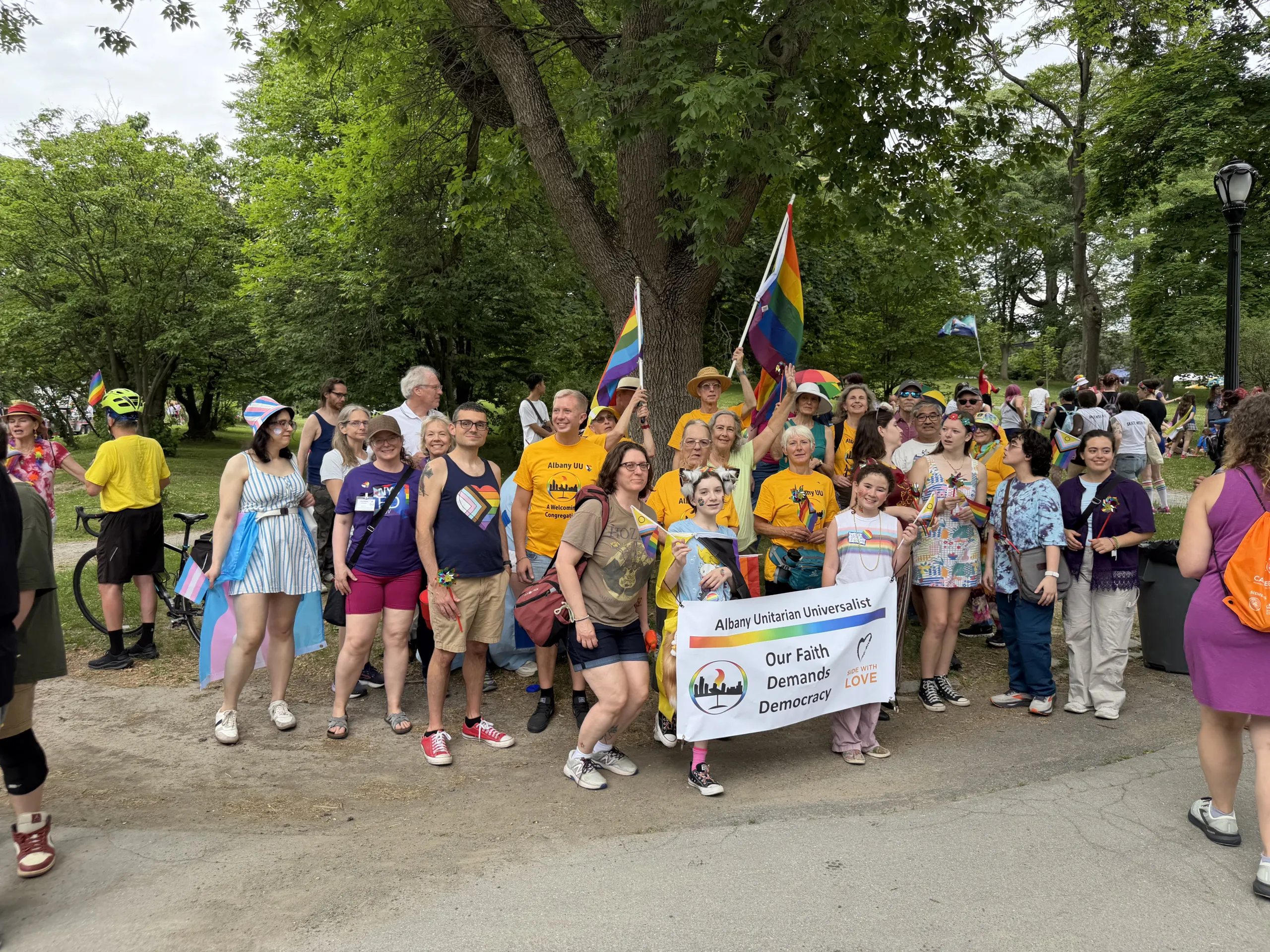 A group of Albany Unitarian Universalist marchers posing together with pride flags under a tree