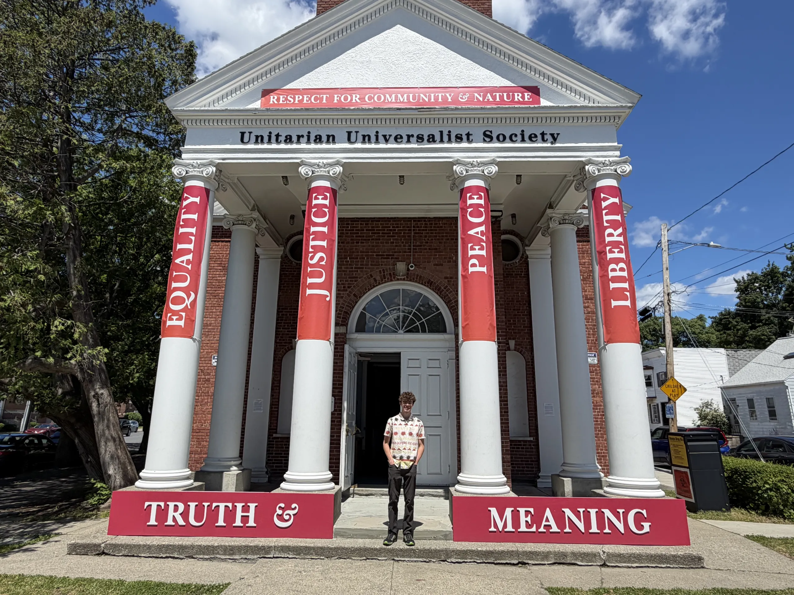 A young man standing in front of the Unitarian Universalist Society building with its red pillar banners
