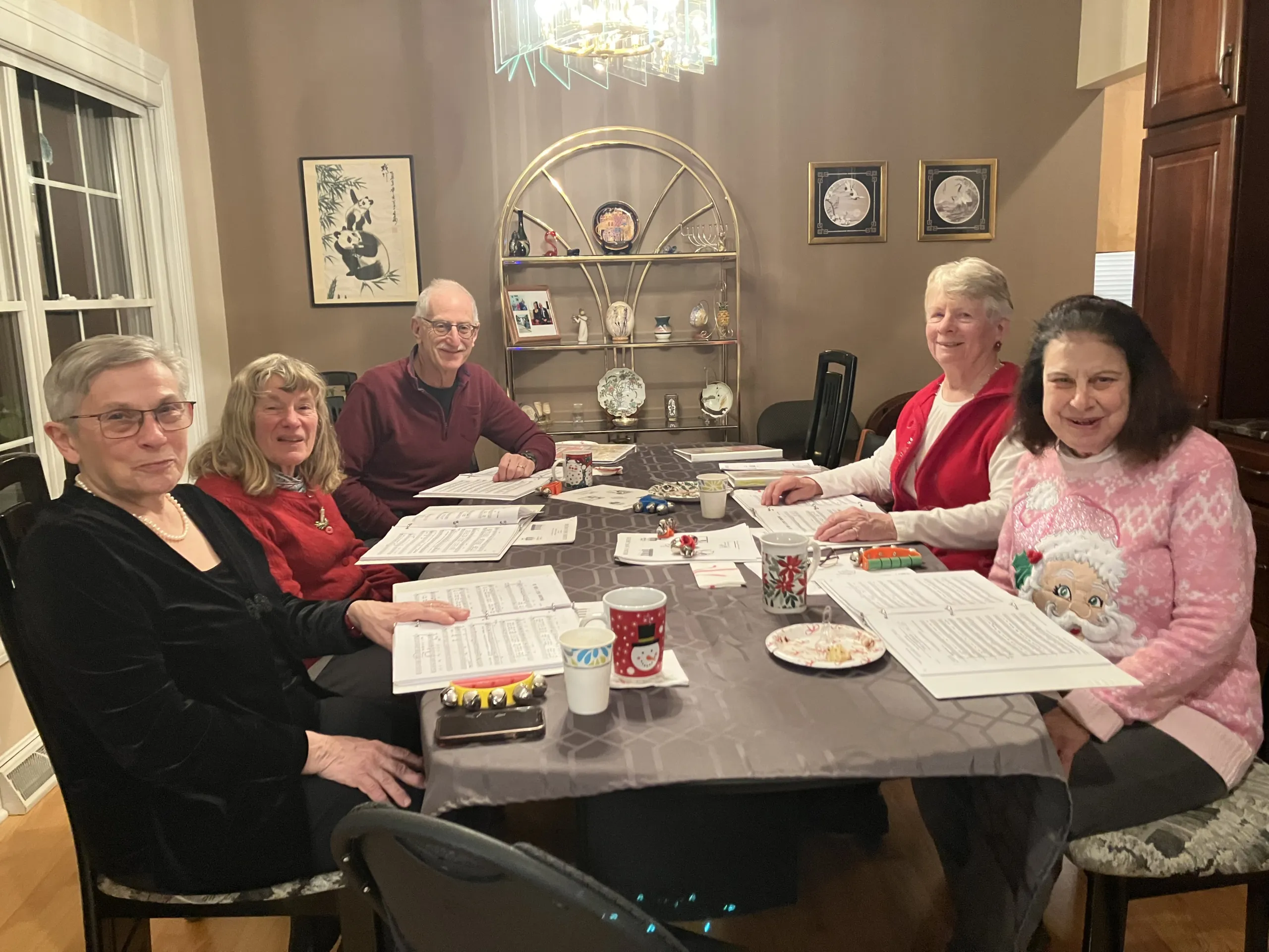Five people seated at a dinner table with sheet music, mugs, and smiles during an auction dinner event