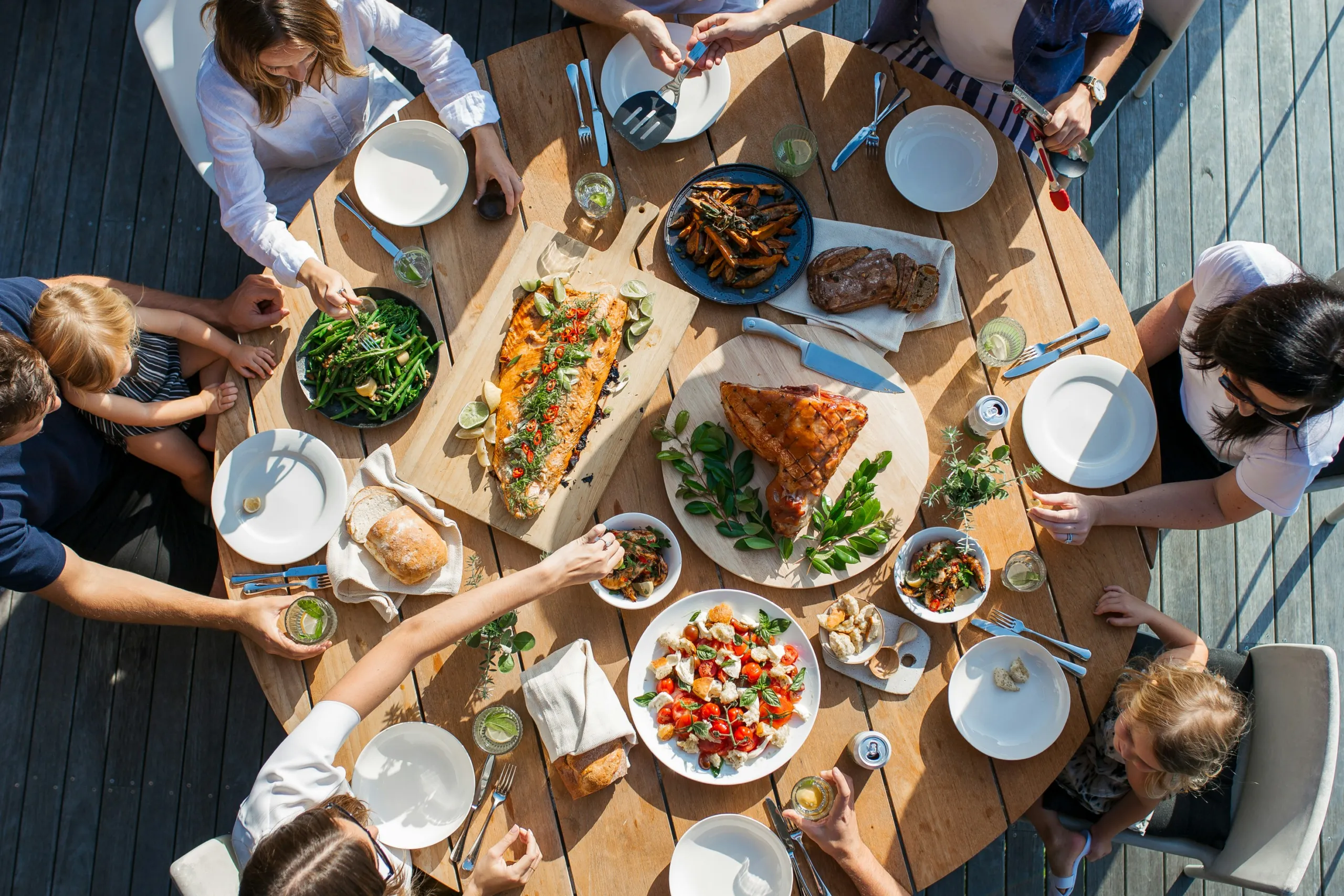 Overhead view of a table with roasted salmon, chicken, salads, and bread shared outdoors