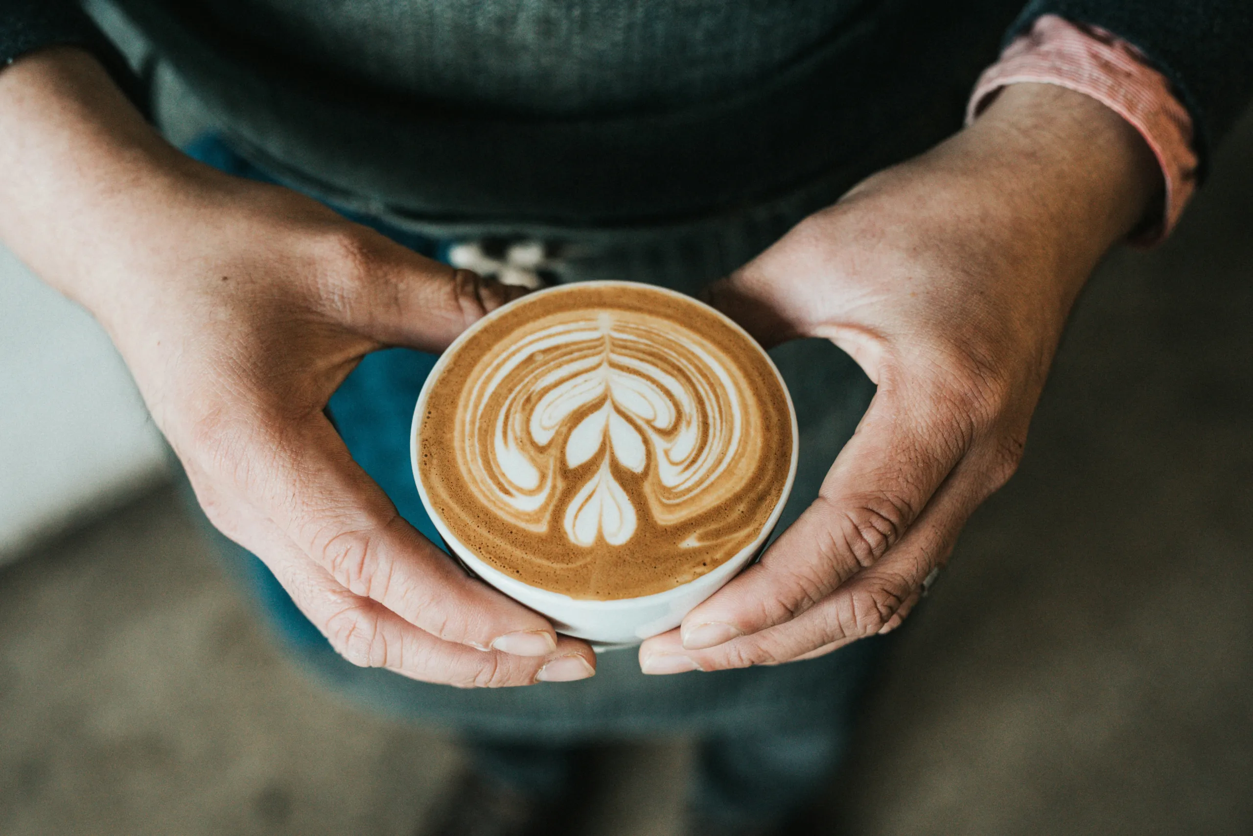 A person holding a cup of coffee with latte art in both hands