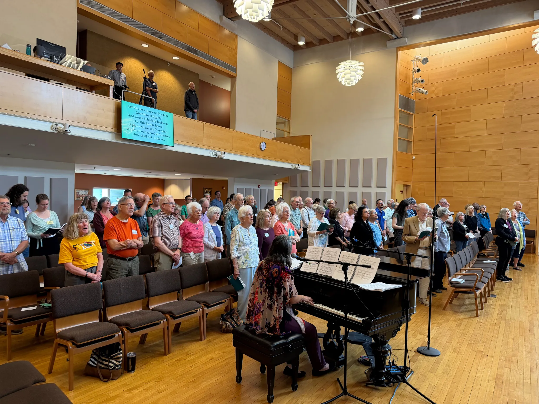 Congregation members standing and singing together as a pianist plays