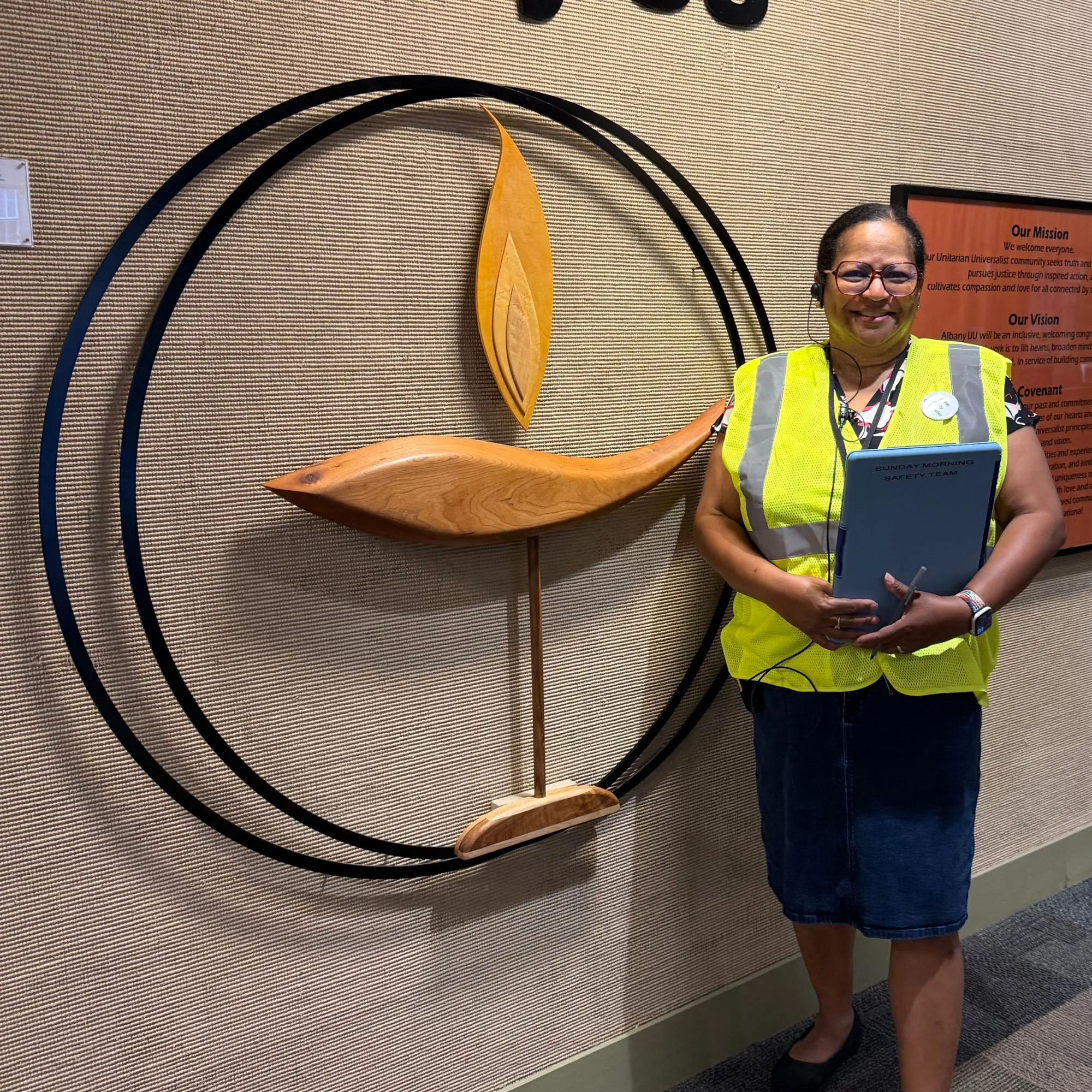 A safety team volunteer in a yellow vest standing beside a wooden flaming chalice sculpture