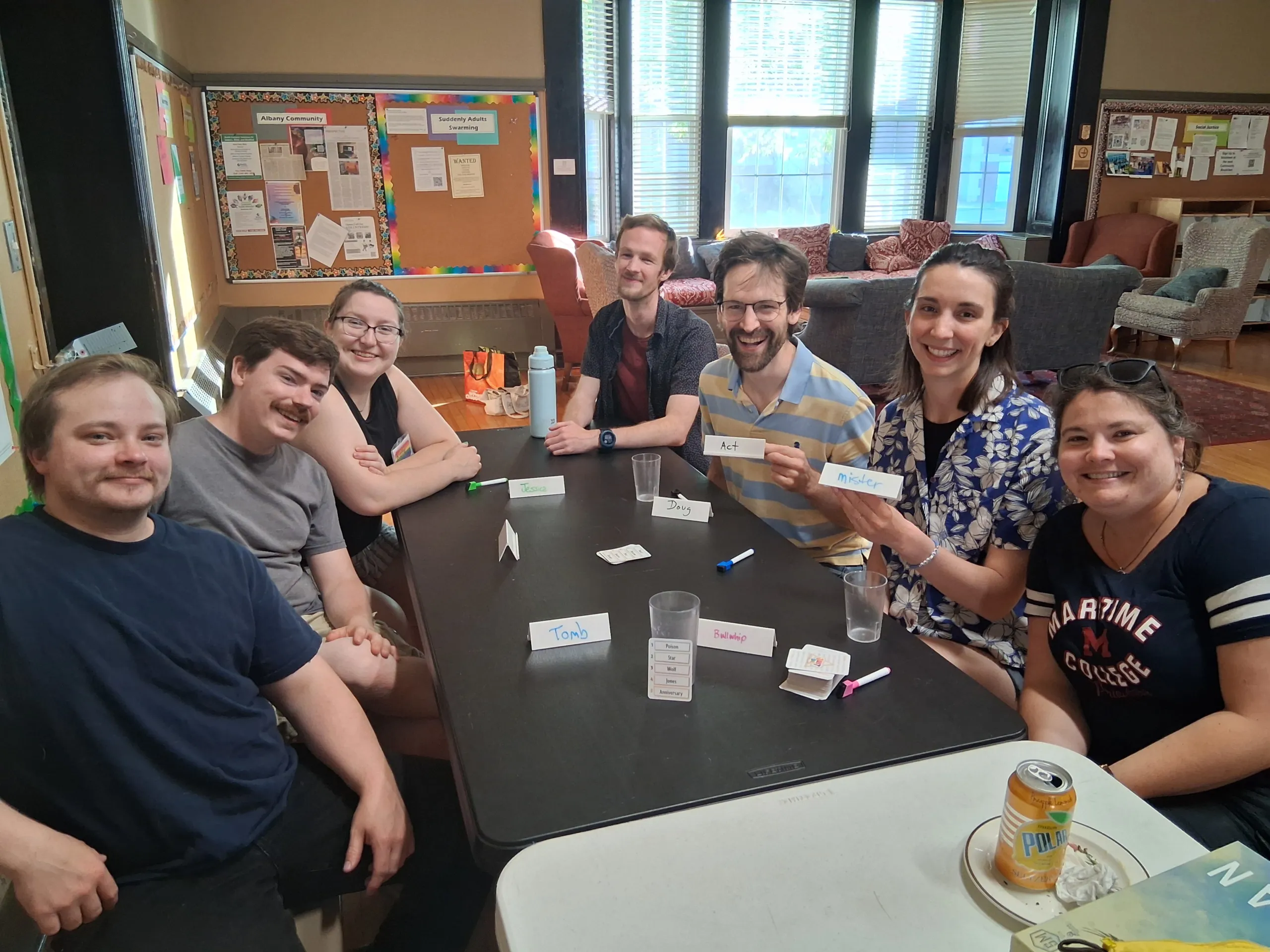 Young adults smiling around a table playing a word-guessing game with name cards