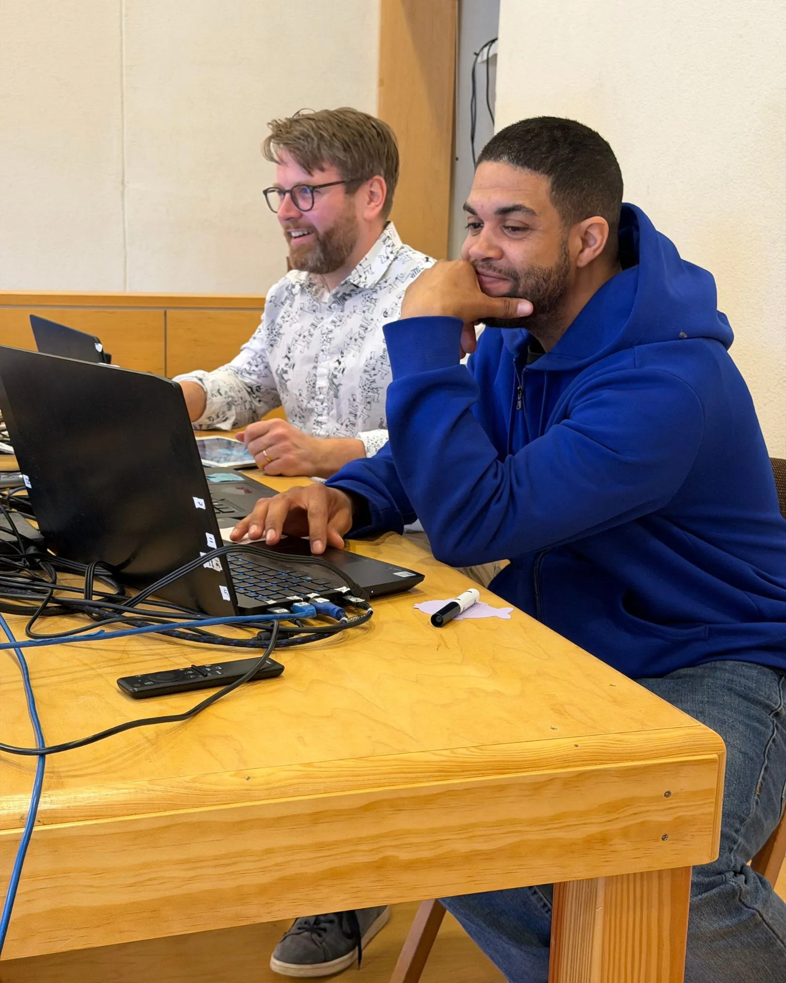 Two men at a table looking at laptops during a tech setup