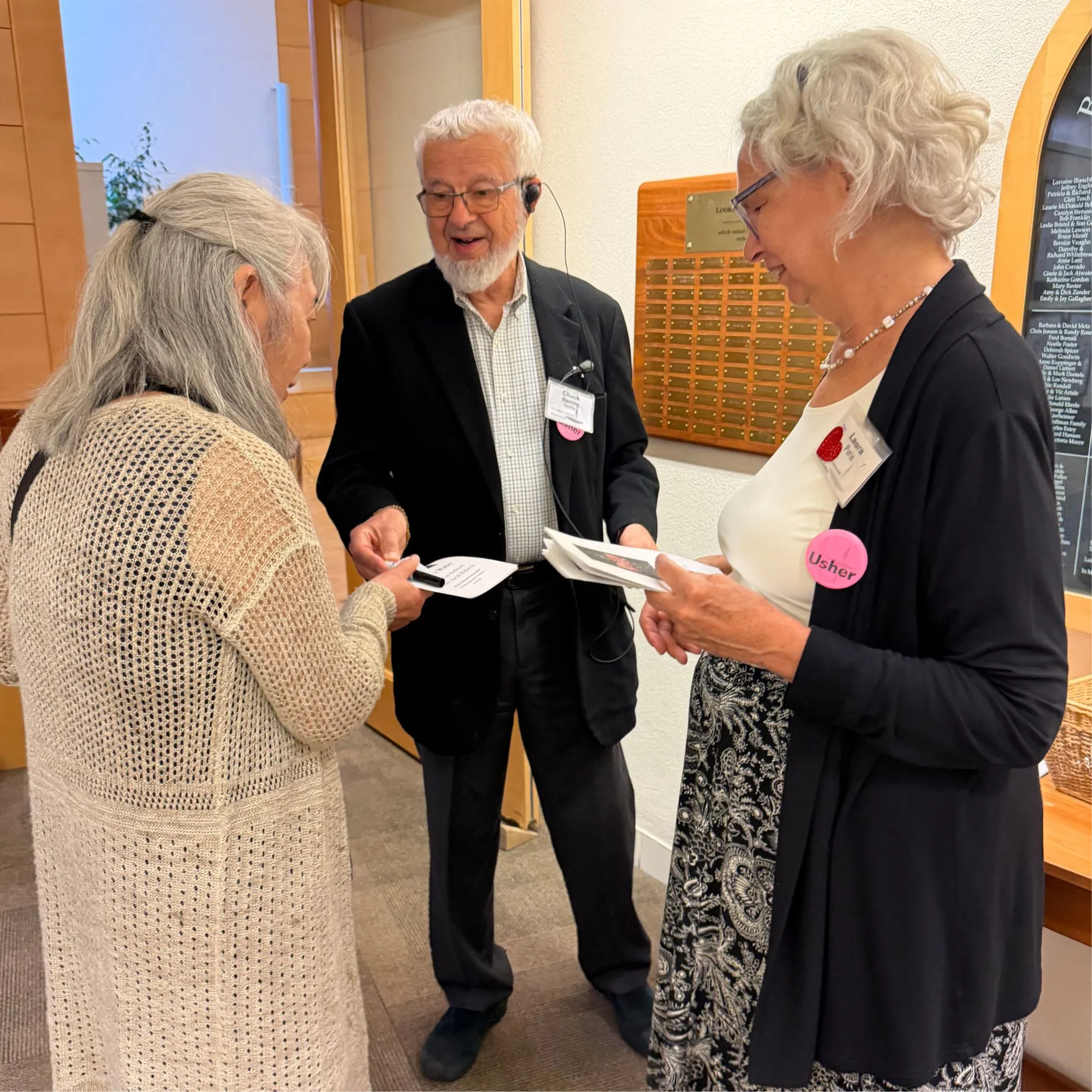 Three ushers exchanging programs and greeting each other in a lobby