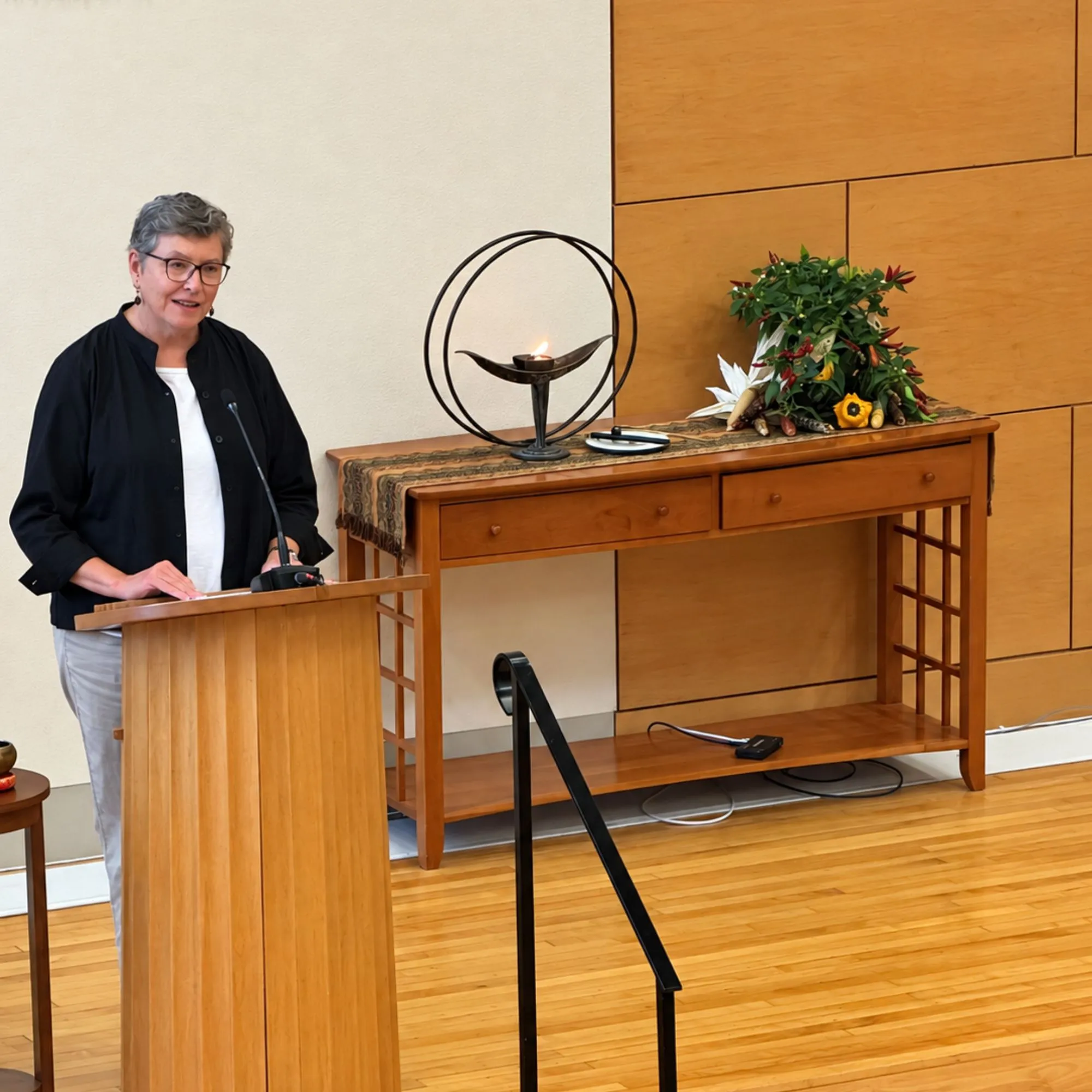 A worship associate speaking at a podium beside a lit chalice and flower arrangement