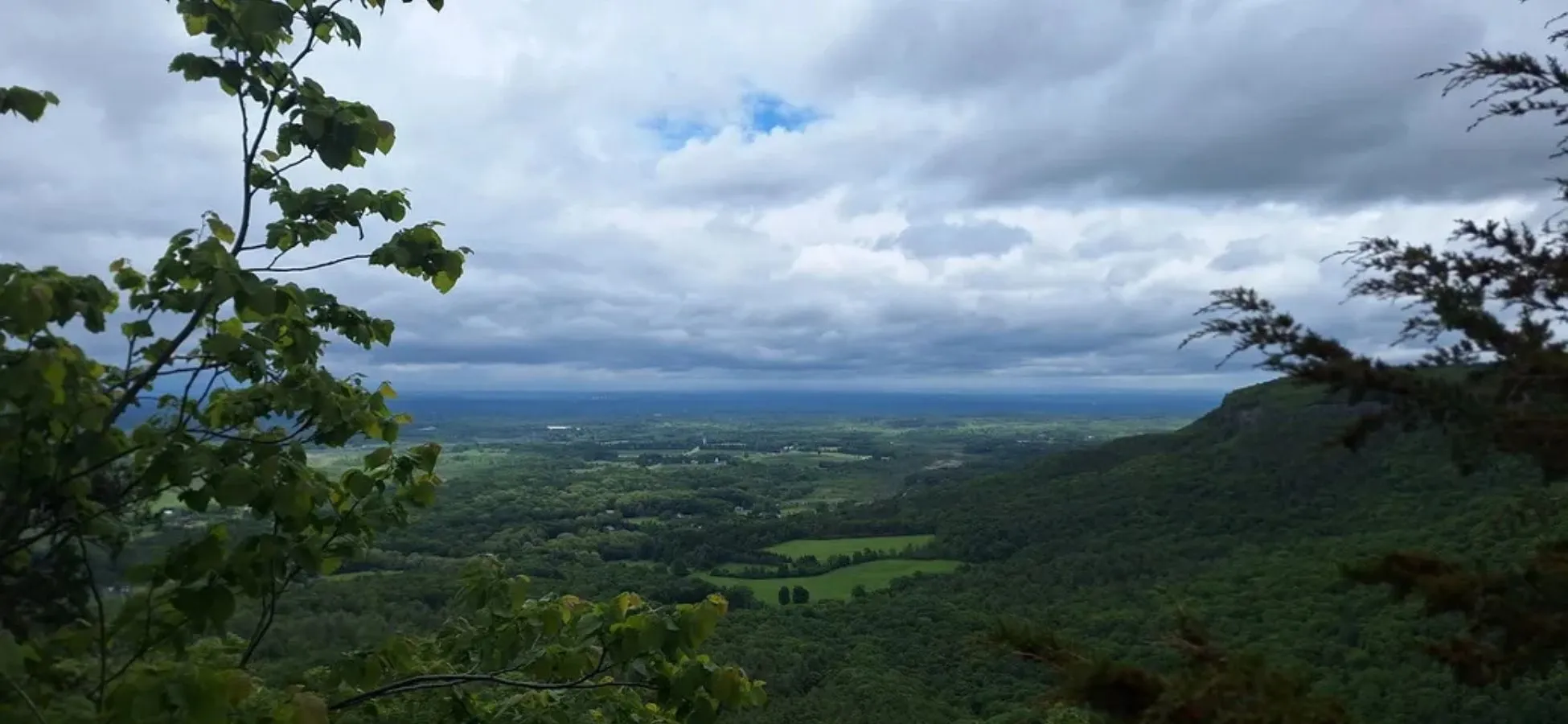 View over a green forested valley beneath a cloudy sky from a rocky overlook at Thacher State Park